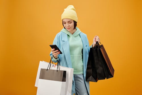 Gratis Mujer Con Gorro De Punto Amarillo Y Abrigo Verde Con Bolsa De Papel Blanco Foto de stock